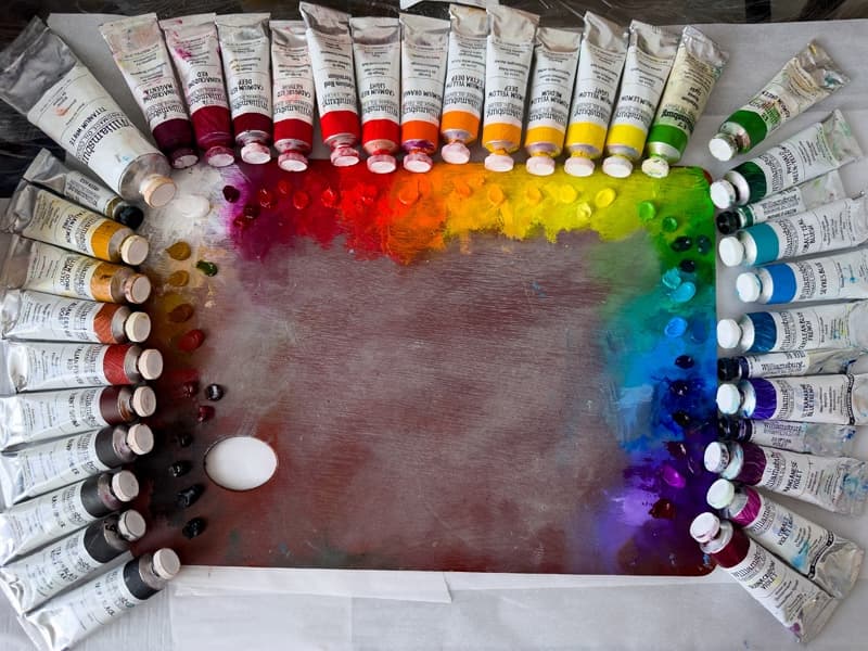 An array of Williamsburg paint tubes around a wooden palette.