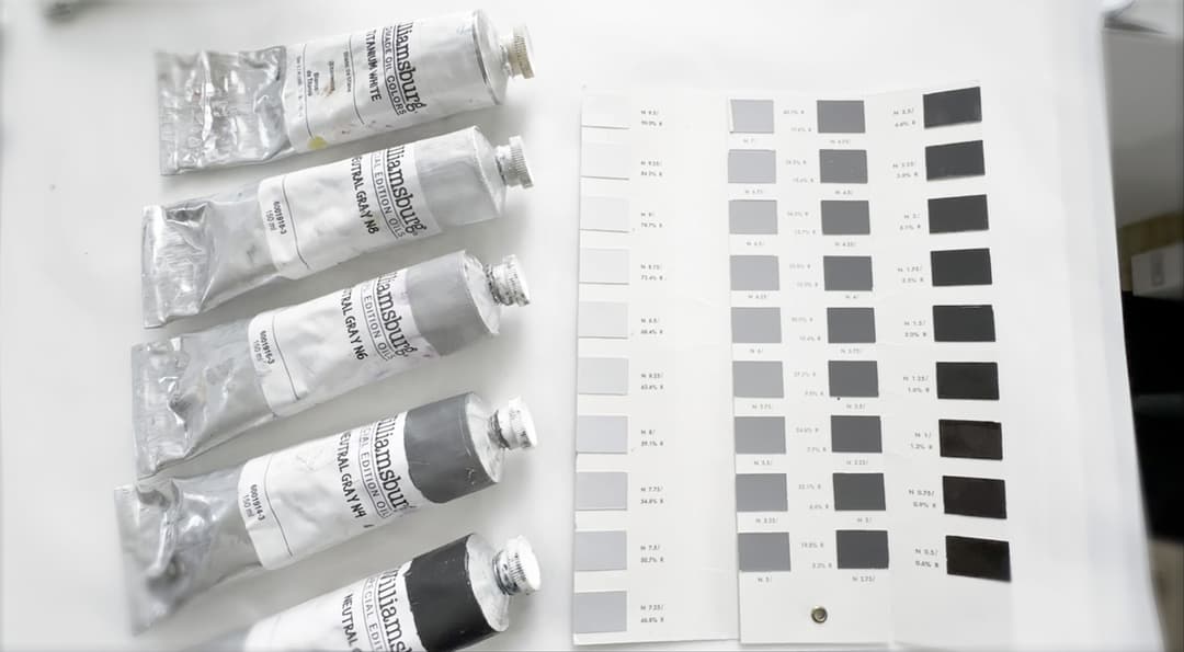 A set of grey swatches calibrated to the Munsell system next to four tubes of oil paint.