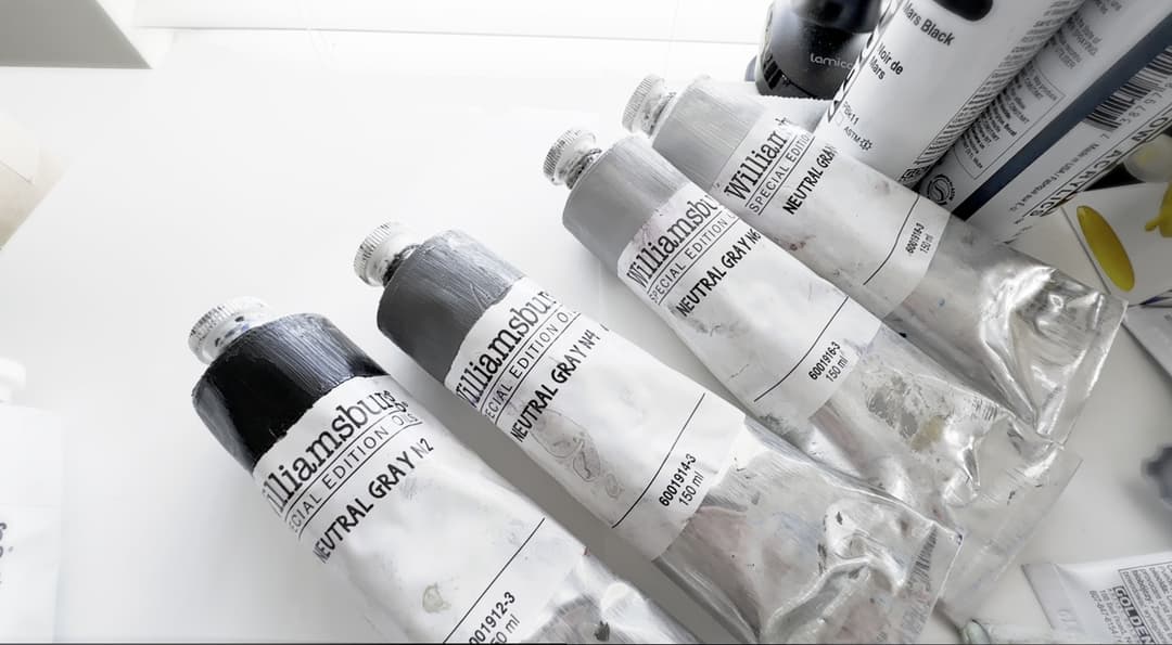 Four tubes of oil paint in deepening shades of grey.