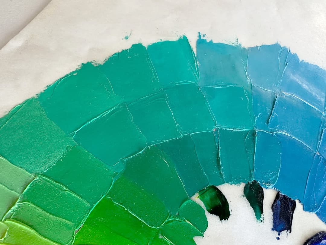 A section of a painted color wheel showing swatches of green paint progressing more toward blue.
