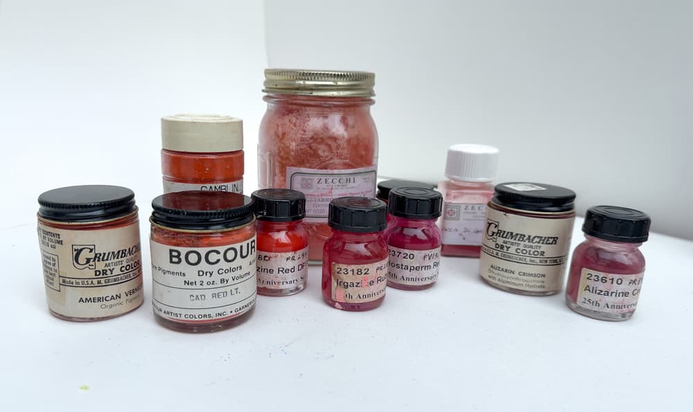 An array of red pigments in jars. The image illustrates a few of the red pigments available to artists.