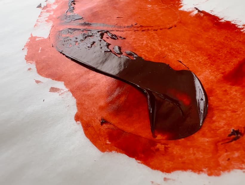 A stroke of paint made with a palette knife, a deep brown Quinacridone Burnt Scarlet with rich red-orange where the paint is thin