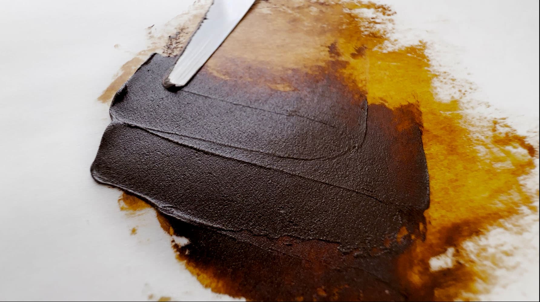 A swatch of brown oil paint which looks gold when spread thinly